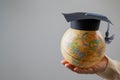 Woman holding a globe wearing a graduation cap.