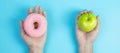 Woman holding green apple and pink donut, female choose between fruit is Healthy food and sweet is unhealthy junk foods. Dieting, Royalty Free Stock Photo