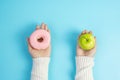 Woman holding green apple and pink donut, female choose between fruit is Healthy food and sweet is unhealthy junk foods. Dieting, Royalty Free Stock Photo