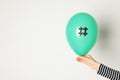 Woman holding green balloon with paper hashtag symbol on white background, closeup