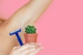 A woman holding a green cactus in a brown pot and a razor near the armpits. the concept of depilation, hair removal and