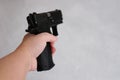 Woman holding gun in her hand at home. Focus hand of young women using black gun on gray background Royalty Free Stock Photo