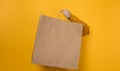 Woman holding in hand brown blank craft paper bag for takeaway on yellow background. Packaging template mock up. Delivery service Royalty Free Stock Photo