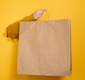 Woman holding in hand brown blank craft paper bag for takeaway on yellow background. Packaging template Royalty Free Stock Photo