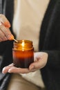 Woman holding in hand candle and light candle in small amber glass jar with wooden wick. Zen and relax concept Royalty Free Stock Photo