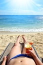 Woman holding in hand glass with drink and lying on a sun lounger on sandy beach. Royalty Free Stock Photo