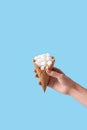 Woman holding in hand ice-cream wafer cone filled with white sugar cubes isolated on blue background Royalty Free Stock Photo