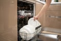 Woman holding in hand plate and getting out or putting in it in kithen or dishwasher shelf.