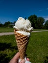 Woman holding in hand a Vanilla ice-cream balls in a waffer cone starting to melt in park with green landscape and blue sky Royalty Free Stock Photo