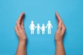 Woman holding hands around paper silhouette of family on light blue background, top view. Insurance concept Royalty Free Stock Photo