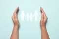 Woman holding hands around paper silhouette of family on light blue background, top view. Insurance concept Royalty Free Stock Photo