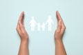 Woman holding hands around paper silhouette of family on light blue background, top view. Insurance concept Royalty Free Stock Photo