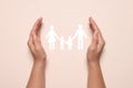 Woman holding hands around paper silhouette of family on light pink background, top view. Insurance concept Royalty Free Stock Photo