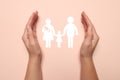 Woman holding hands around paper silhouette of family on pink background, top view. Insurance concept Royalty Free Stock Photo