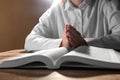 Woman holding hands clasped while praying over Bible at wooden table, closeup Royalty Free Stock Photo