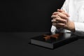 Woman holding hands clasped while praying at table with Bible against black background, closeup. Space for text Royalty Free Stock Photo