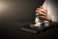 Woman holding hands clasped while praying at table with Bible and cross against dark background, closeup. Space for text Royalty Free Stock Photo