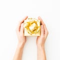 Woman holding in hands golden gift box. Holiday concept on white background. Flat lay. Top view