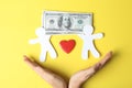 Woman holding hands near paper silhouettes of people, heart and money bills on color background, top view. Royalty Free Stock Photo