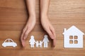 Woman holding hands over paper silhouette of family on wooden background, top view.