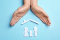 Woman holding hands over paper silhouettes of family and house roof on color background, top view.