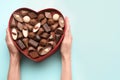 Woman holding heart shaped box with delicious chocolate candies on light blue background, top view. Space for text Royalty Free Stock Photo
