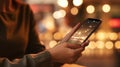 Woman is holding her cell phone in front of her. She appears to be looking at it while standing near lighted area or setting