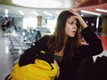 woman holding her head waiting airport yellow backpack tired