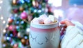 Woman holding hot chocolate in front of Christmas tree. Royalty Free Stock Photo