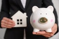 Woman holding house model against white background, focus on piggy bank Royalty Free Stock Photo