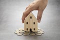 Woman holding a house model rests on a lot of coin on gray table background