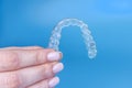 Hand holding removable invisible transparent aligner invisalign or plastic orthodontic braces retainer on blue