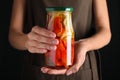 Woman holding jar with pickled bell peppers against black background