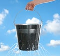 Woman holding leaky bucket with water against sky, closeup Royalty Free Stock Photo