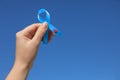 Woman holding light blue ribbon with paper blood drop against sky, closeup. Diabetes awareness