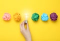 Woman holding lightbulb among colorful paper balls on yellow background, top view. Idea concept Royalty Free Stock Photo