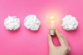 Woman holding lightbulb among paper balls on pink background, top view. Idea concept Royalty Free Stock Photo