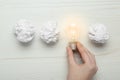 Woman holding lightbulb among paper balls at white wooden table, top view. Idea concept Royalty Free Stock Photo