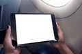 Woman holding and looking at black tablet pc with blank white desktop screen next to an airplane window with clouds and sky backgr Royalty Free Stock Photo