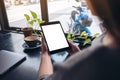 A woman holding and looking at black tablet pc with blank white desktop screen with notebook, green leaves and coffee cup on woode Royalty Free Stock Photo