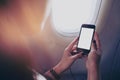 Woman holding and looking at smart phone with blank white screen next to an airplane window Royalty Free Stock Photo