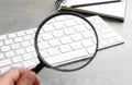 Woman holding magnifier glass near keyboard at grey stone table, closeup. Find keywords concept Royalty Free Stock Photo