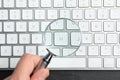 Woman holding magnifier glass over keyboard on slate table, top view. Find keywords concept Royalty Free Stock Photo