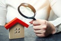 A woman is holding a magnifying glass over a wooden house. Real estate appraiser. Assessment of the condition of the house. Royalty Free Stock Photo