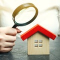 A woman is holding a magnifying glass over a wooden house. Real estate appraiser. Assessment of the condition of the house.