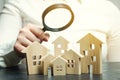 A woman is holding a magnifying glass over a wooden houses. Real estate appraiser. Property valuation / appraisal. Find a house.