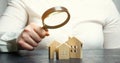 A woman is holding a magnifying glass over a wooden houses. Real estate appraiser. Property valuation / appraisal. Find a house. Royalty Free Stock Photo