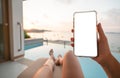 Woman holding mobile phone with blank screen while laying on sunbathing bed with beach view Royalty Free Stock Photo