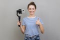 Woman holding mobile phone and steadicam looking at camera with positive expression showing thumb up Royalty Free Stock Photo