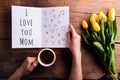 Woman holding Mothers day greeting and coffee. Yellow tulips. Royalty Free Stock Photo